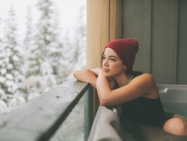 Woman sitting in a hot tub, looking out at a snowy winter view.